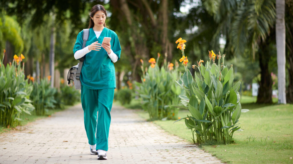 Female Nurse walking through a garden path while using phone.