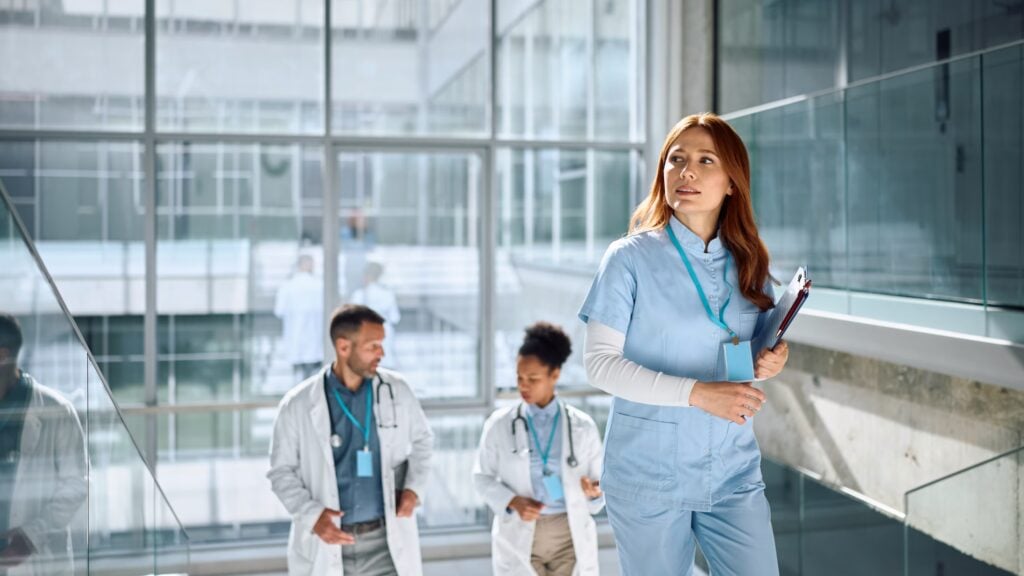 Female nurse walking up stairs inside grand hospital with accompanying doctors behind.