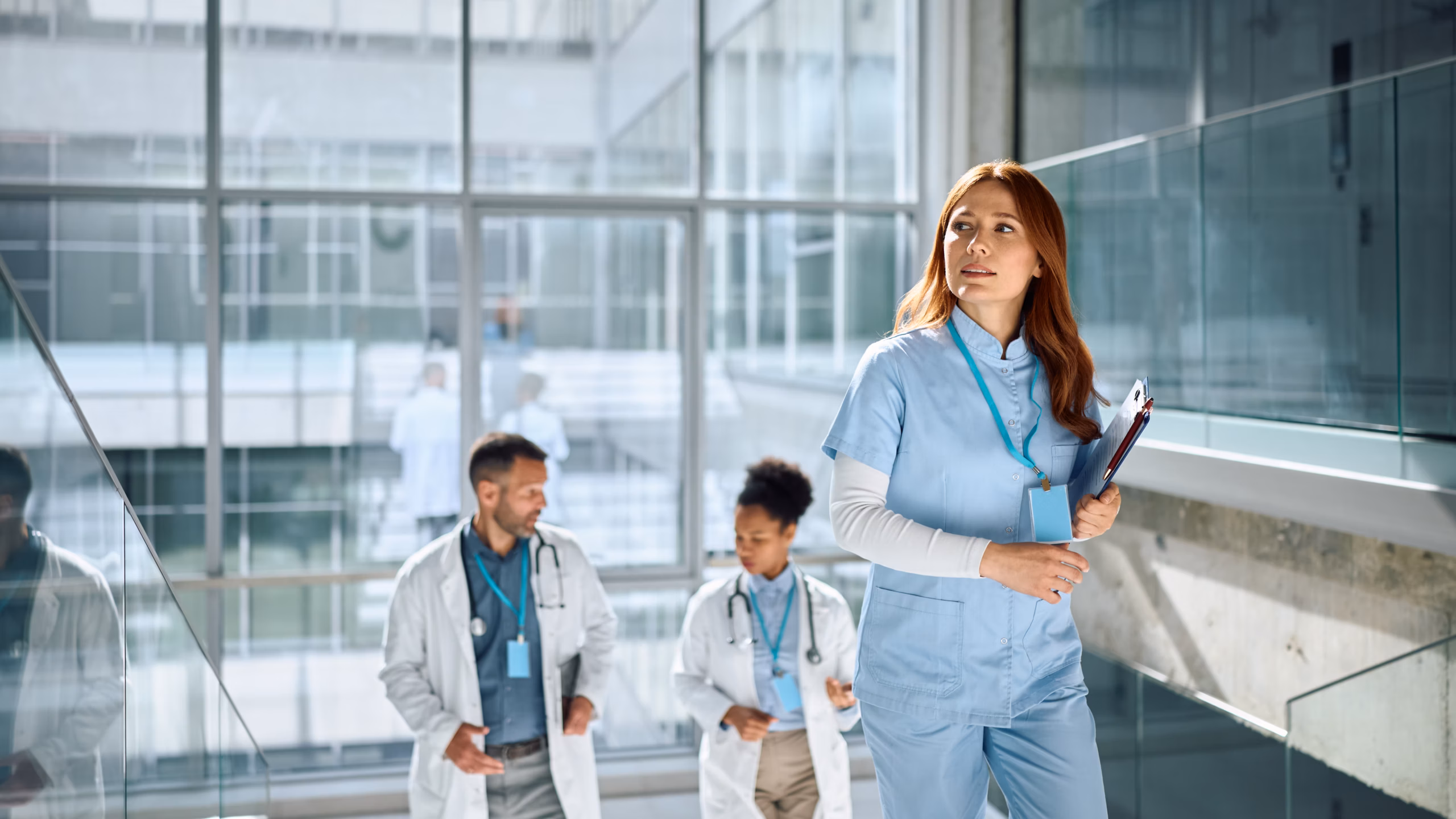 Female nurse walking up stairs inside grand hospital with accompanying doctors behind.
